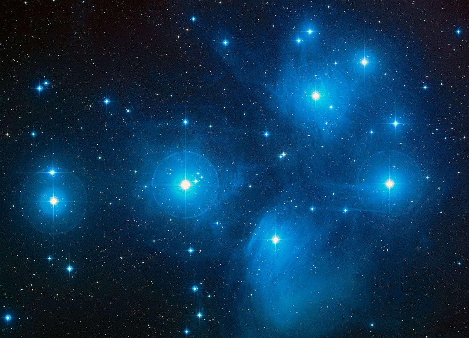Blue-white stars of the Pleiades surrounded by wisps of blue reflection nebulosity